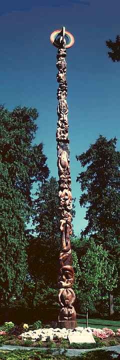 Totem pole by Georganna Malloff, showing stylized people and creatures dancing round a maypole surmounted by a rainbow-painted ring; titled Cosmic Maypole.