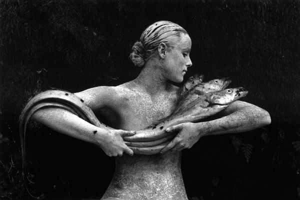 A woman with mottled stonelike skin cradles three eels.