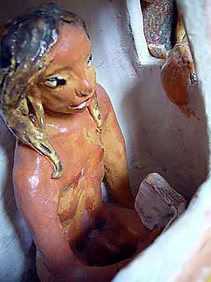 Clay statue: a naked longhaired man reading inside a kiosk.