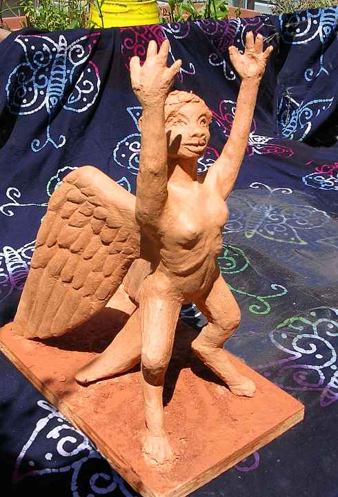 A rearing lebbird woman in profile with her arms raised, showing wings; unfired clay sculpture. Click to enlarge.
