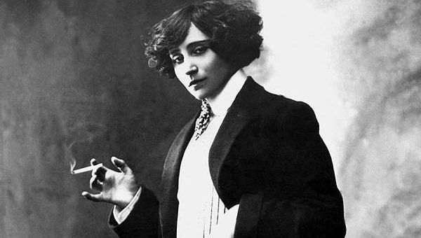 Colette, French writer, in a tux with a cigarette against clouds; black and white photo.